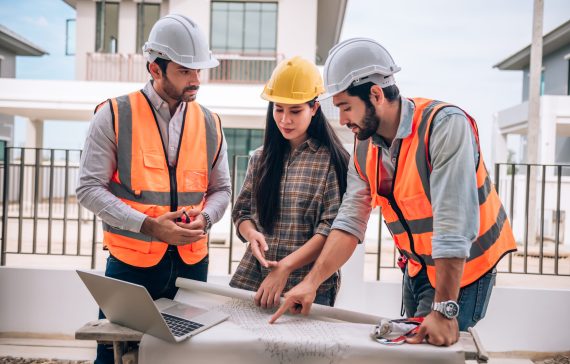 Civil engineer , Construction worker and Architects wearing hardhats and safety vests are working together at construction site ,building ,home in cooperation teamwork concept.