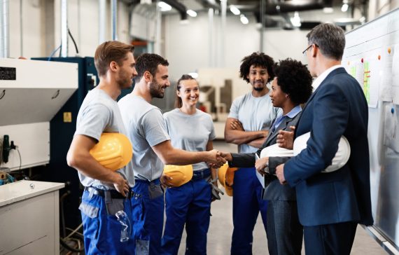 Company managers visiting their employees in a factory. Happy African American businesswoman is shaking hands with one worker.